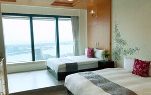 Habitación de hotel con dos camas, un ventanal amplio con vista a la ciudad, un armario de madera y una pared con un mural floral.