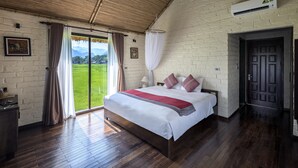Une chambre dotée d’un grand lit, d’un plancher en bois, d’une vue sur un champ verdoyant accessible par une porte coulissante et d’un plafond en bambou.