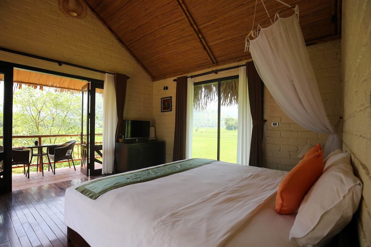 Een slaapkamer met een bed, een televisie en een balkon met een tafel en stoelen.