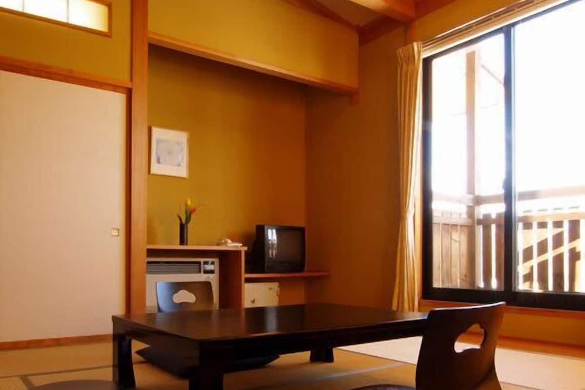 A traditional Japanese room with tatami flooring, a low table, a television, and a sliding door.