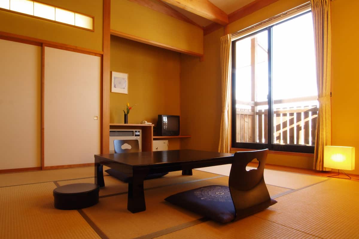 A traditional Japanese room with tatami flooring, a low table, a television, and a sliding door to a balcony.