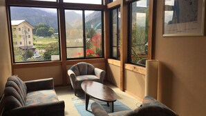 A room with large windows, a sofa, a chair, and a table. - Hakuba Alpine Hotel (Hakuba)