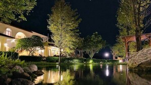 Une vue nocturne d’un étang paisible, avec un bâtiment d’un côté et des arbres de l’autre.