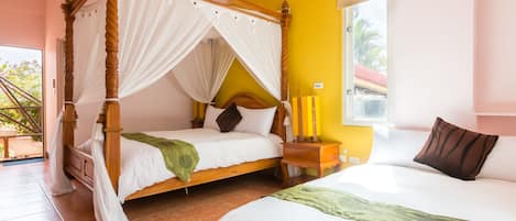 Una cama con dosel con ropa de cama blanca y un edredón verde, una mesita de noche con velas y una ventana con vistas a palmeras.