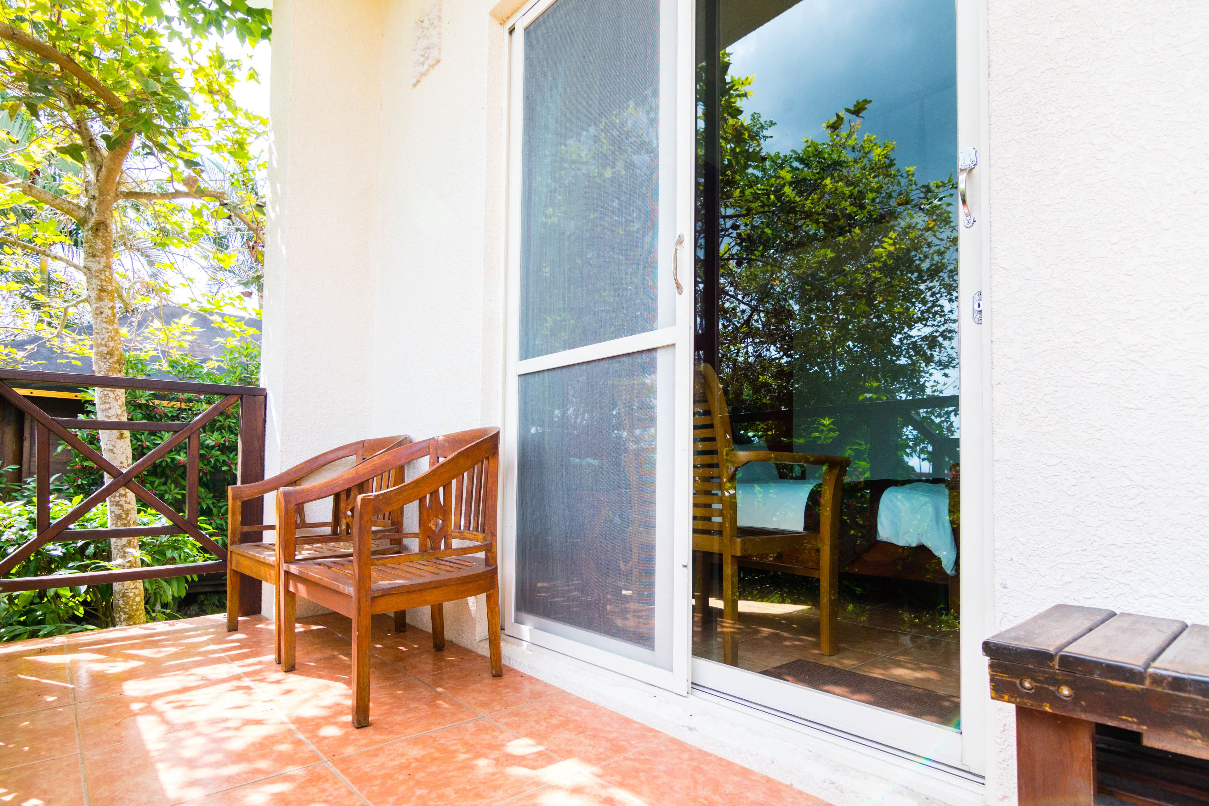 A patio with a wooden bench and a table, a sliding glass door, and a view of a garden.