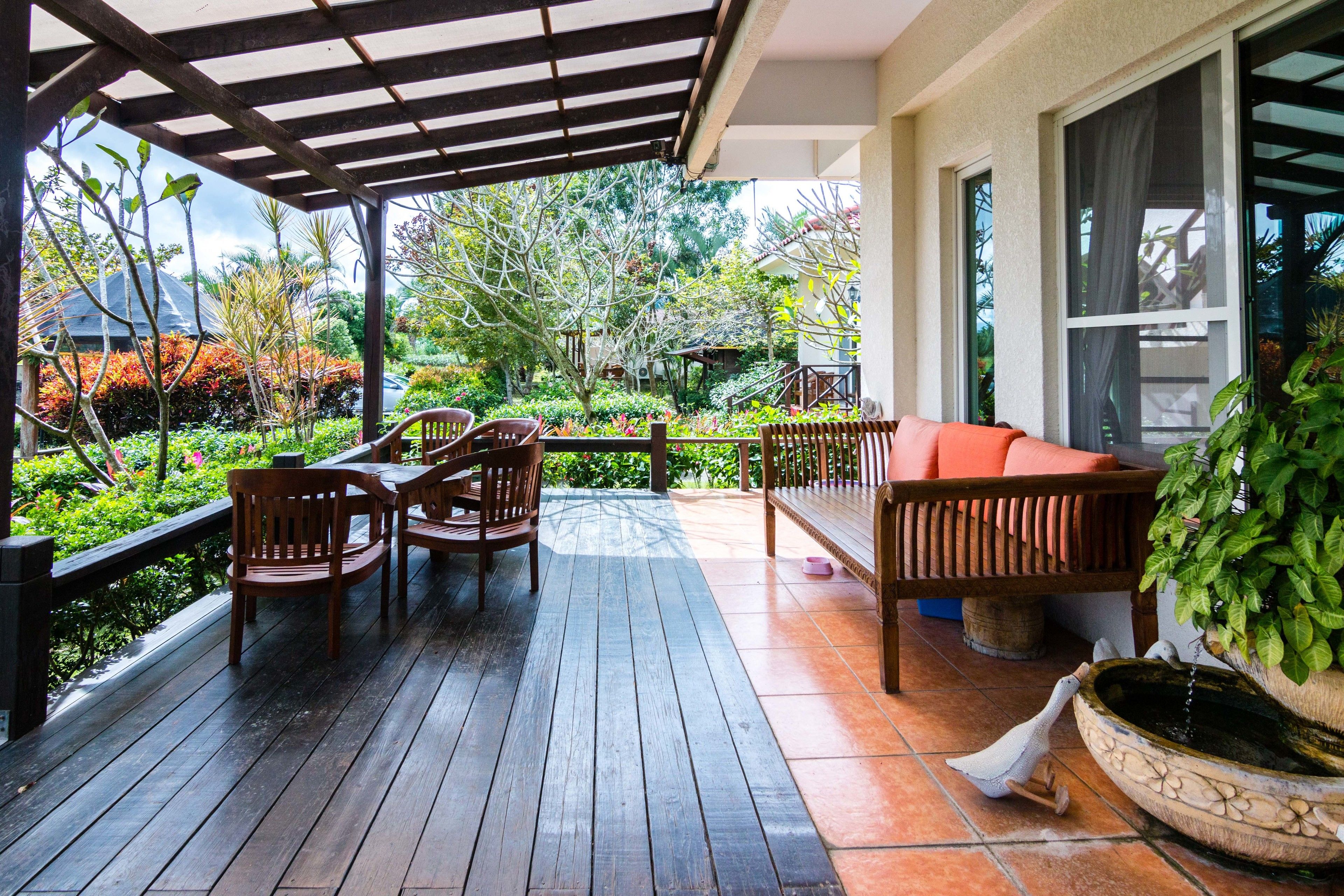 A covered patio with wooden furniture, a water feature, and a view of a garden.