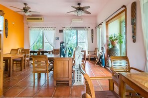 A spacious dining area with wooden furniture, ceiling fans, and large windows with curtains.
