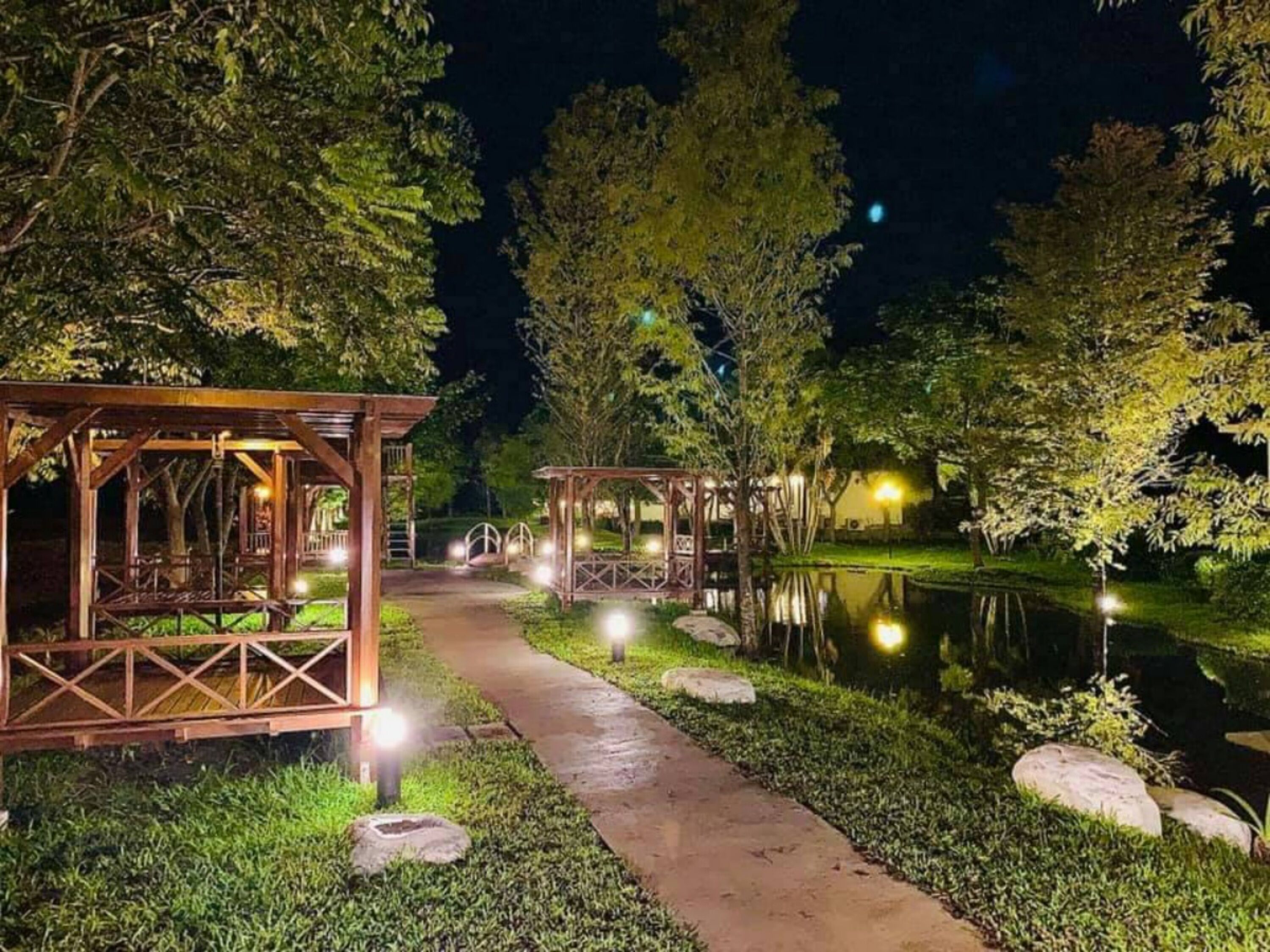 A nighttime outdoor area with wooden gazebos and a pathway leading to a pond.