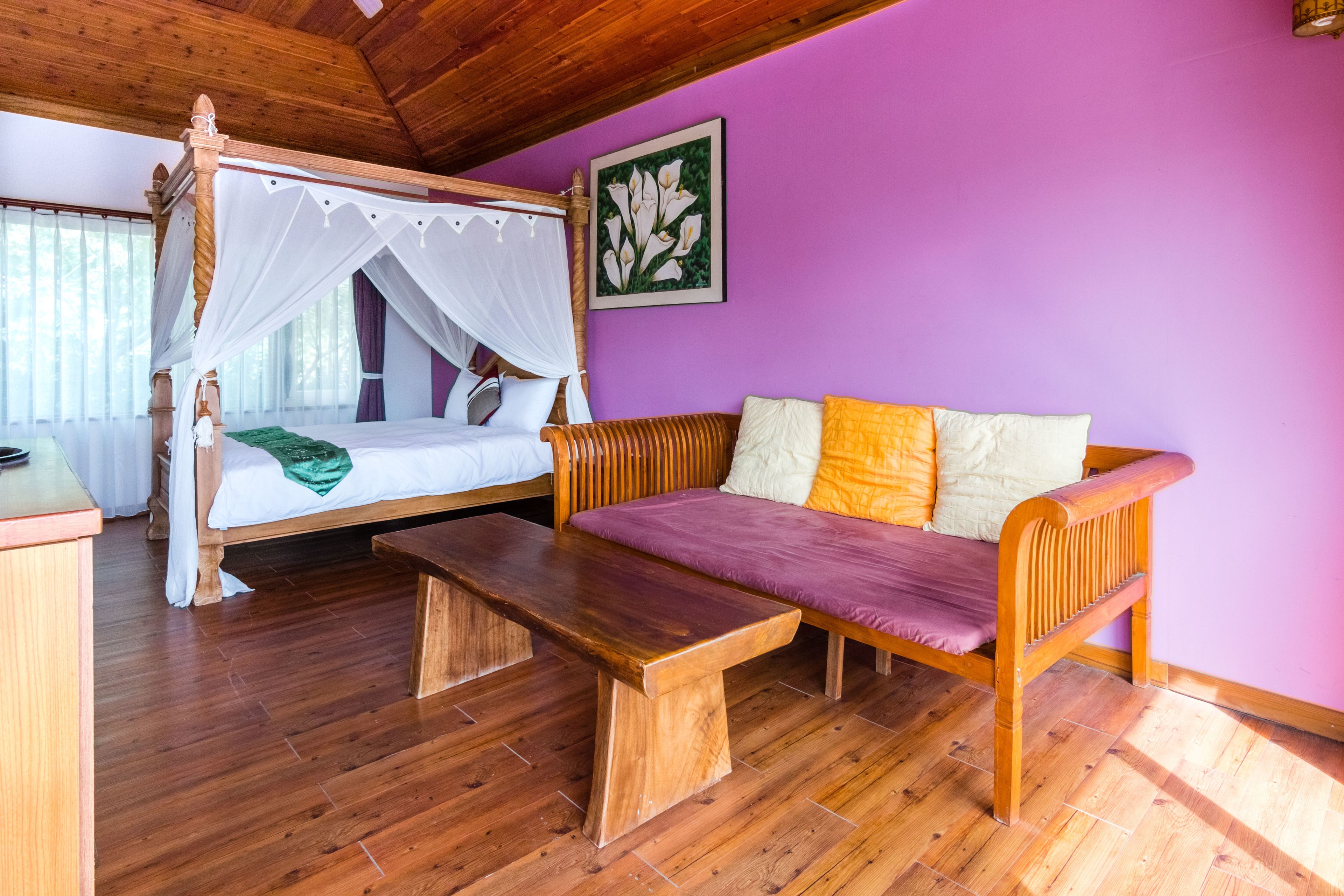 Una habitación con una cama con dosel, un banco de madera y un sofá con cojines.