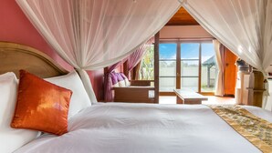 Une chambre à coucher avec un grand lit, une tête de lit en bois et une vue sur l’extérieur grâce à une porte-fenêtre coulissante.