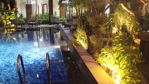 A pool area with lounge chairs and potted plants. - Puri Anom Guest House (Denpasar)