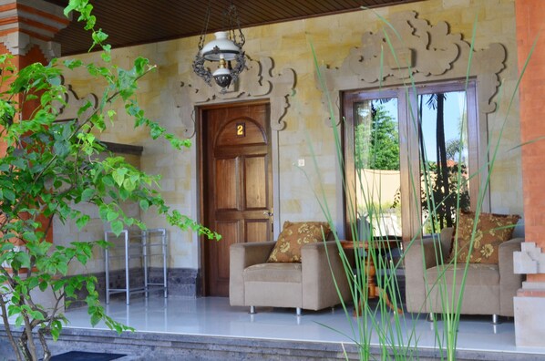 A room with a wooden door marked with the number 2, a sofa with floral cushions, and a hanging light fixture. - Puri Anom Guest House (Denpasar)