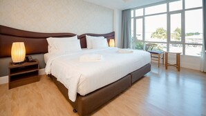 A spacious hotel room with a large bed, a bedside table with a lamp, and a view of the city through large windows. - Avada hotel (Trat)