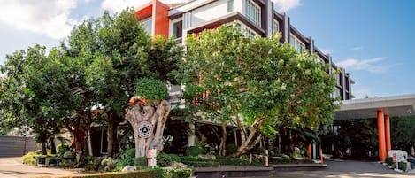 A modern building with a large tree in the foreground, a clear sky, and a well-maintained garden area.