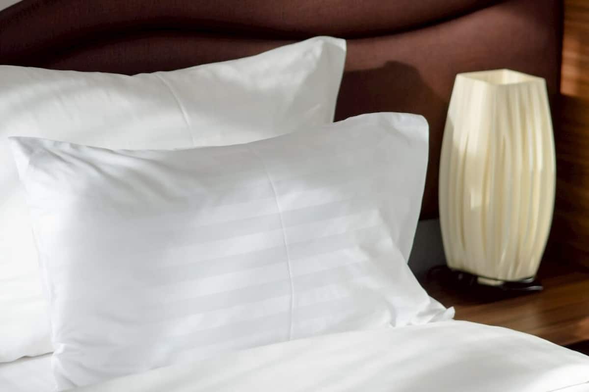Una cama bien hecha con sábanas blancas y un cabecero marrón.