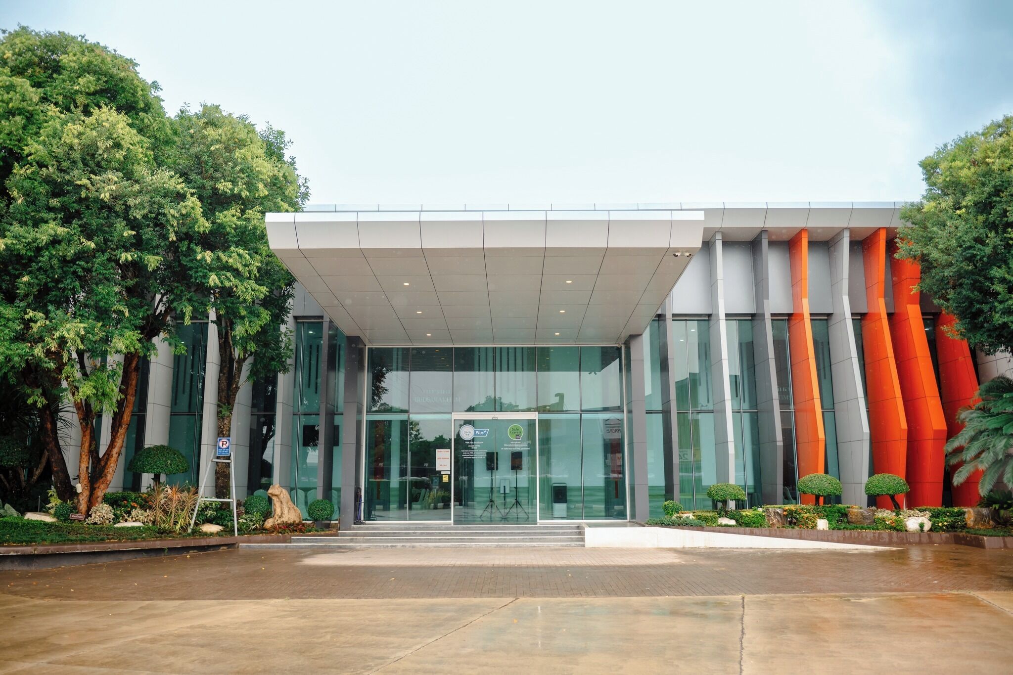 A modern building with a glass entrance, surrounded by greenery and trees.