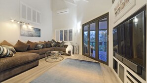 A living room with a sectional sofa, a glass coffee table, and a large TV. There is a sliding glass door leading to an outdoor deck. - Crusoe's Beach House Ocean Views (Cannonvale)