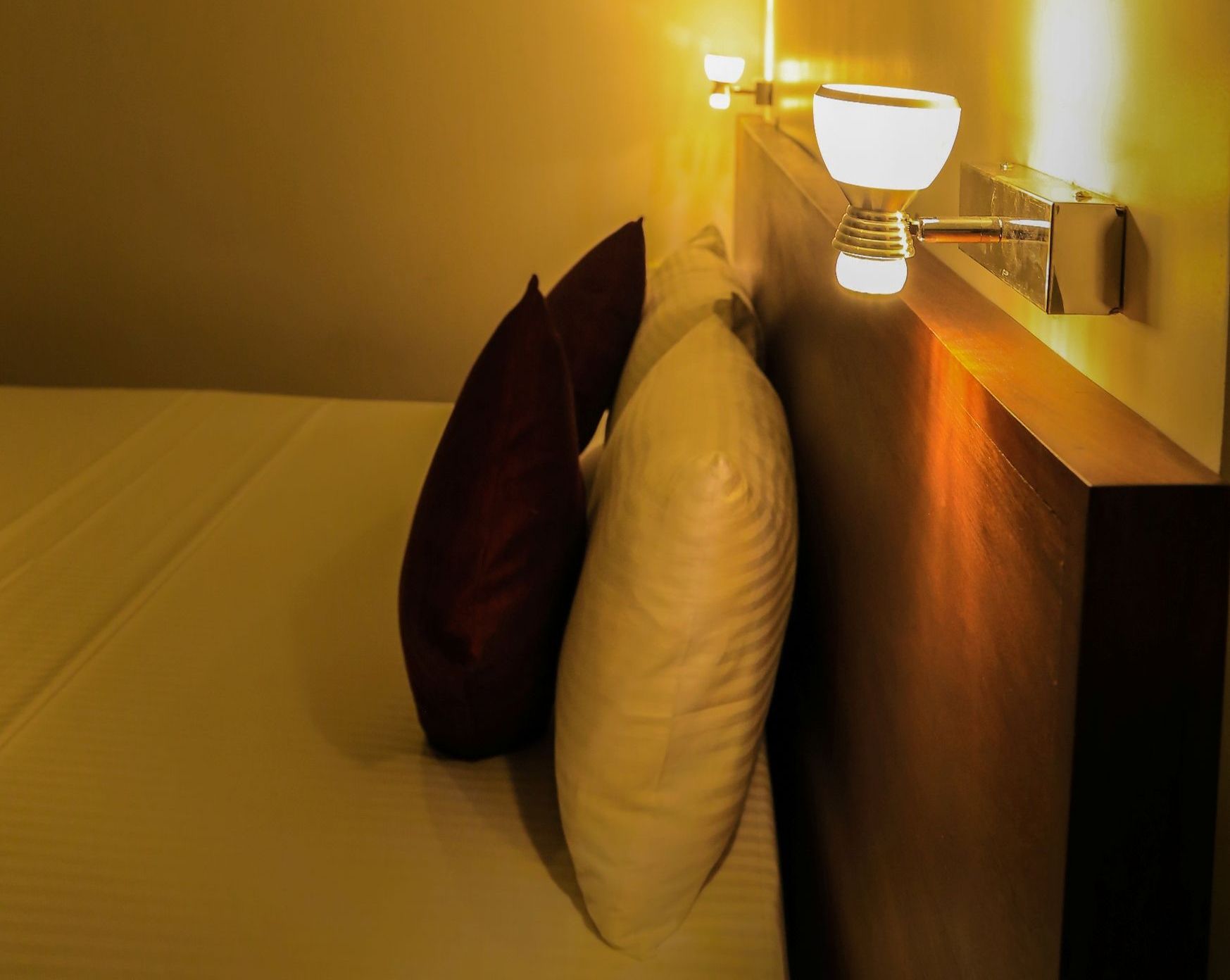 A neatly made bed with a wooden headboard, a bedside lamp, and two pillows.