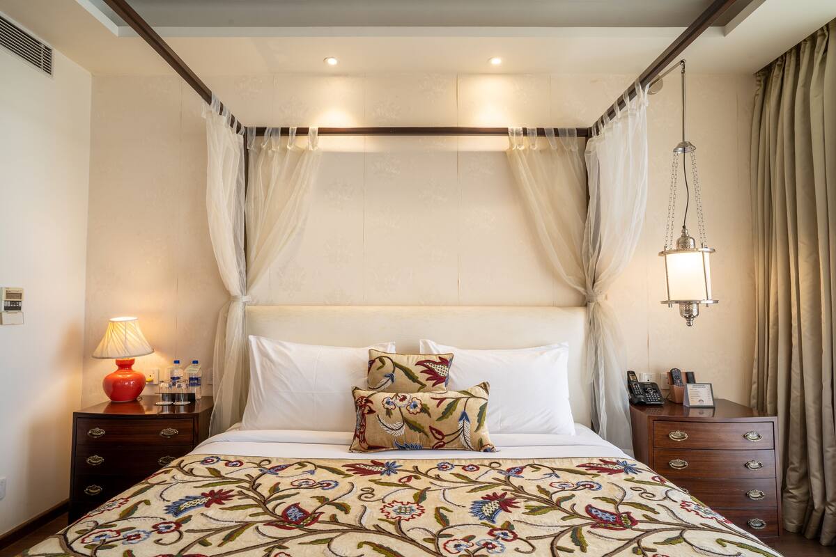 A neatly arranged hotel room with a bed, a bedside table with a lamp, a nightstand with a phone and a lamp, and a hanging light fixture.
