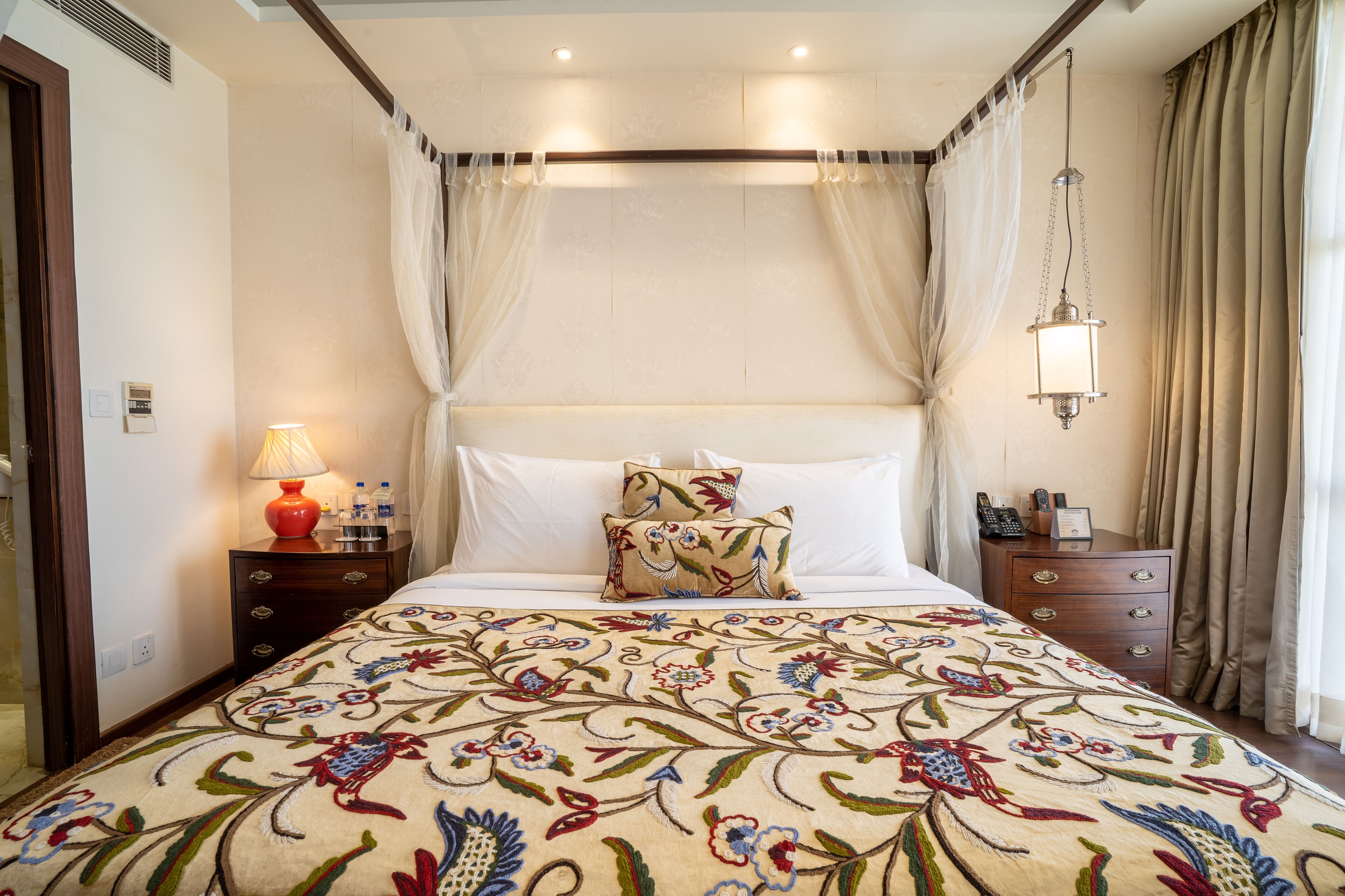 A neatly arranged bedroom with a floral bedspread, a bedside lamp, and a nightstand with a lamp and phone.