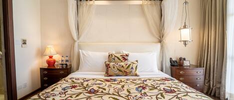 A neatly arranged bedroom with a floral bedspread, a bedside lamp, and a nightstand with a lamp and phone.