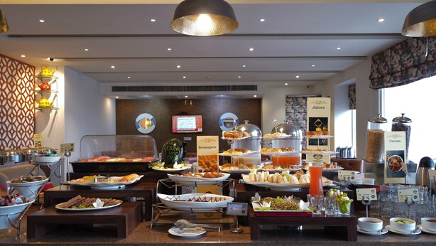 Un'area buffet con diverse postazioni gastronomiche, tra cui una dedicata a succhi e cereali, e una postazione caffè con tazze multiple e distributore di caffè in polvere.