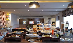 A buffet area with various food stations, including a section for juices and cereals, and a coffee station with multiple cups and a coffee powder dispenser.