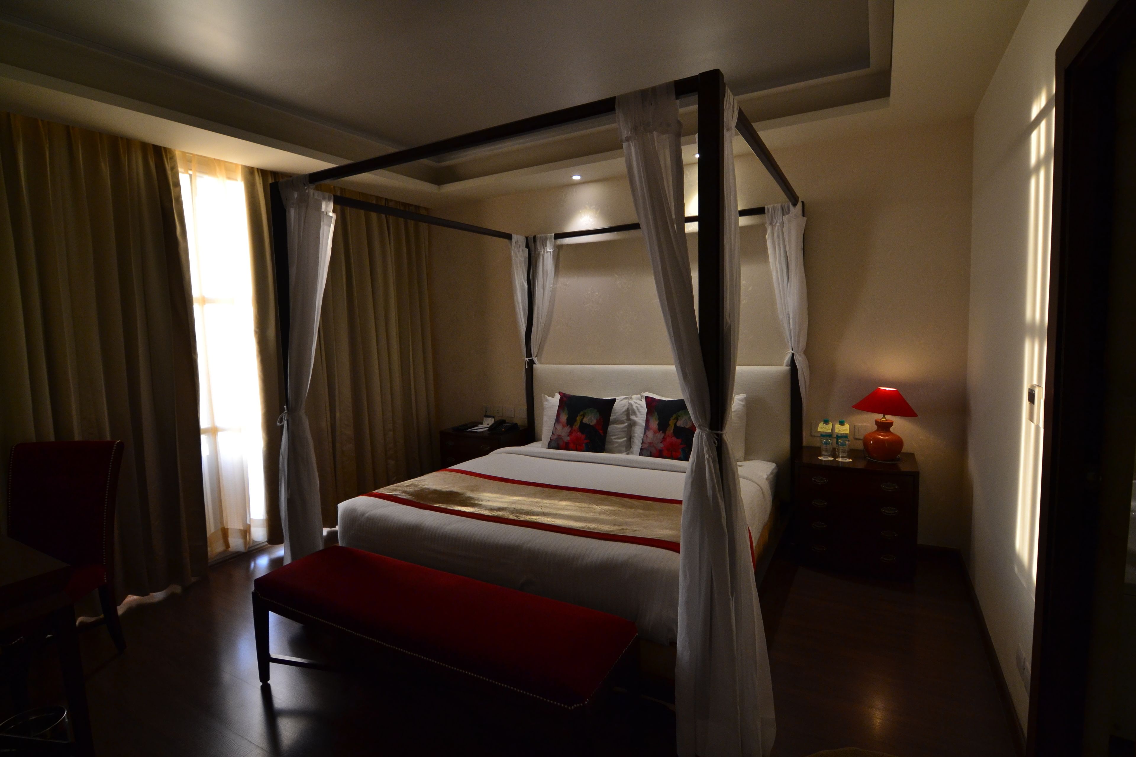 A four-poster bed with a canopy, a bedside table with a lamp, a chair, and a bench.