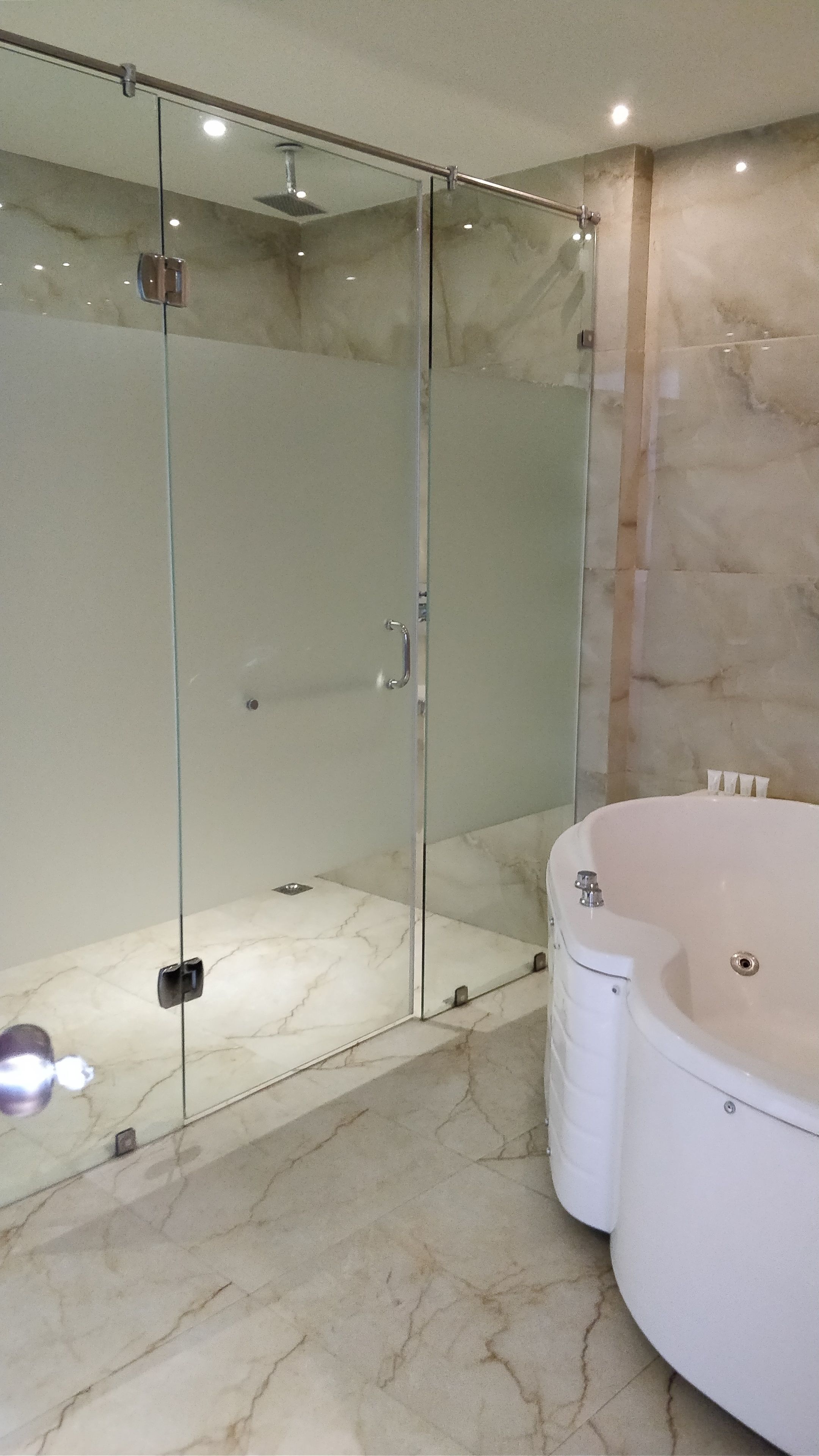 A modern bathroom with a glass-enclosed shower, a marble floor, and a large bathtub.