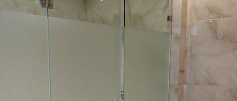 A modern bathroom with a glass-enclosed shower, a marble floor, and a large bathtub.