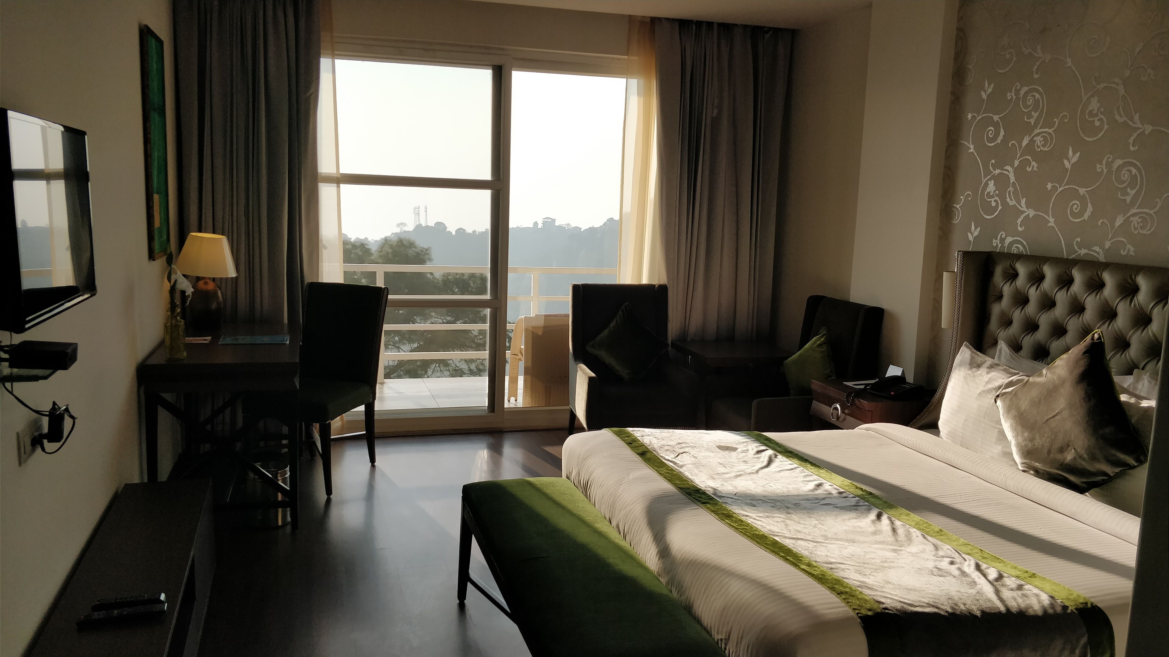 A hotel room with a bed, a desk, a chair, and a view of the cityscape through the window.