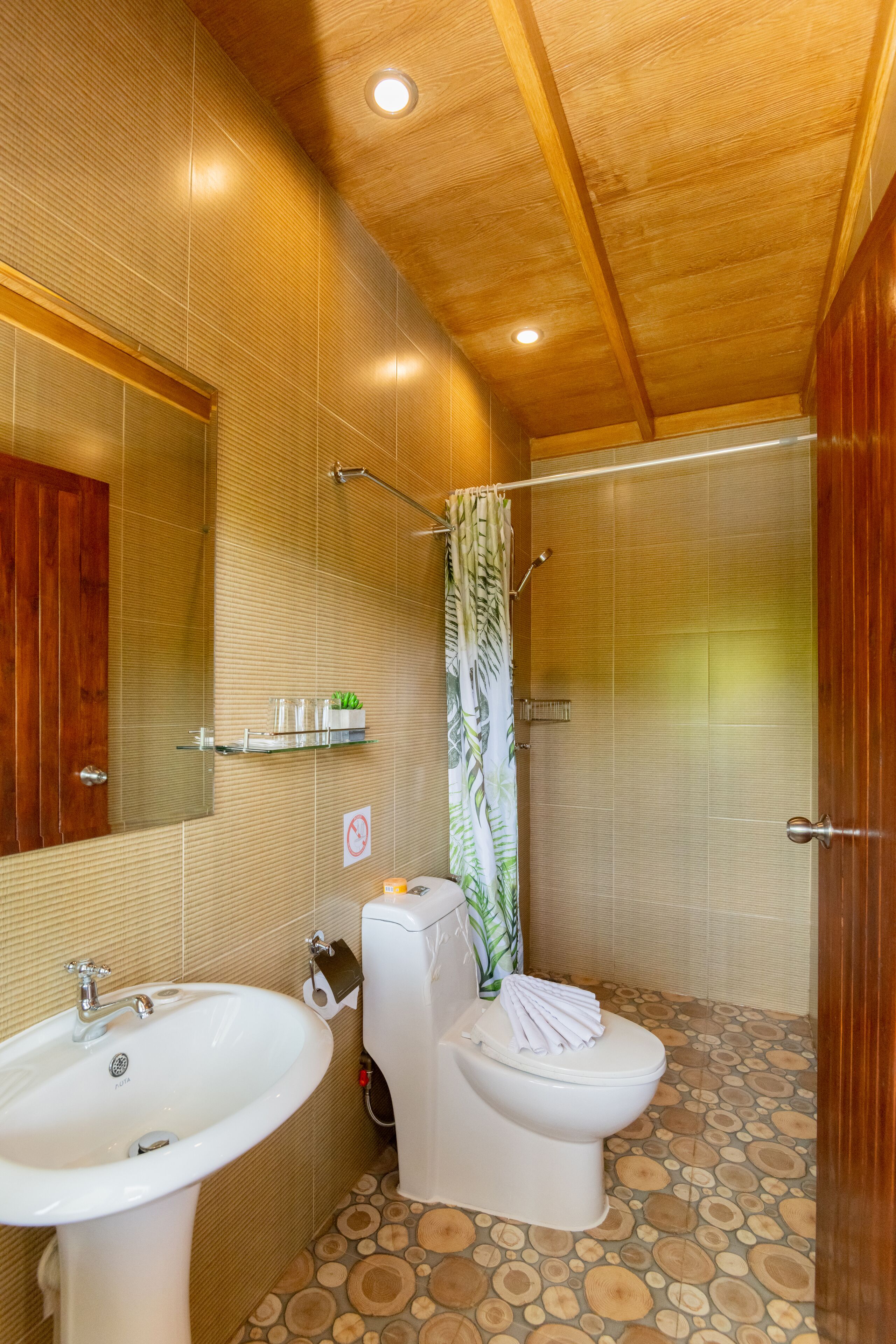 A bathroom with a wooden ceiling, a sink, a toilet, and a shower with a curtain.
