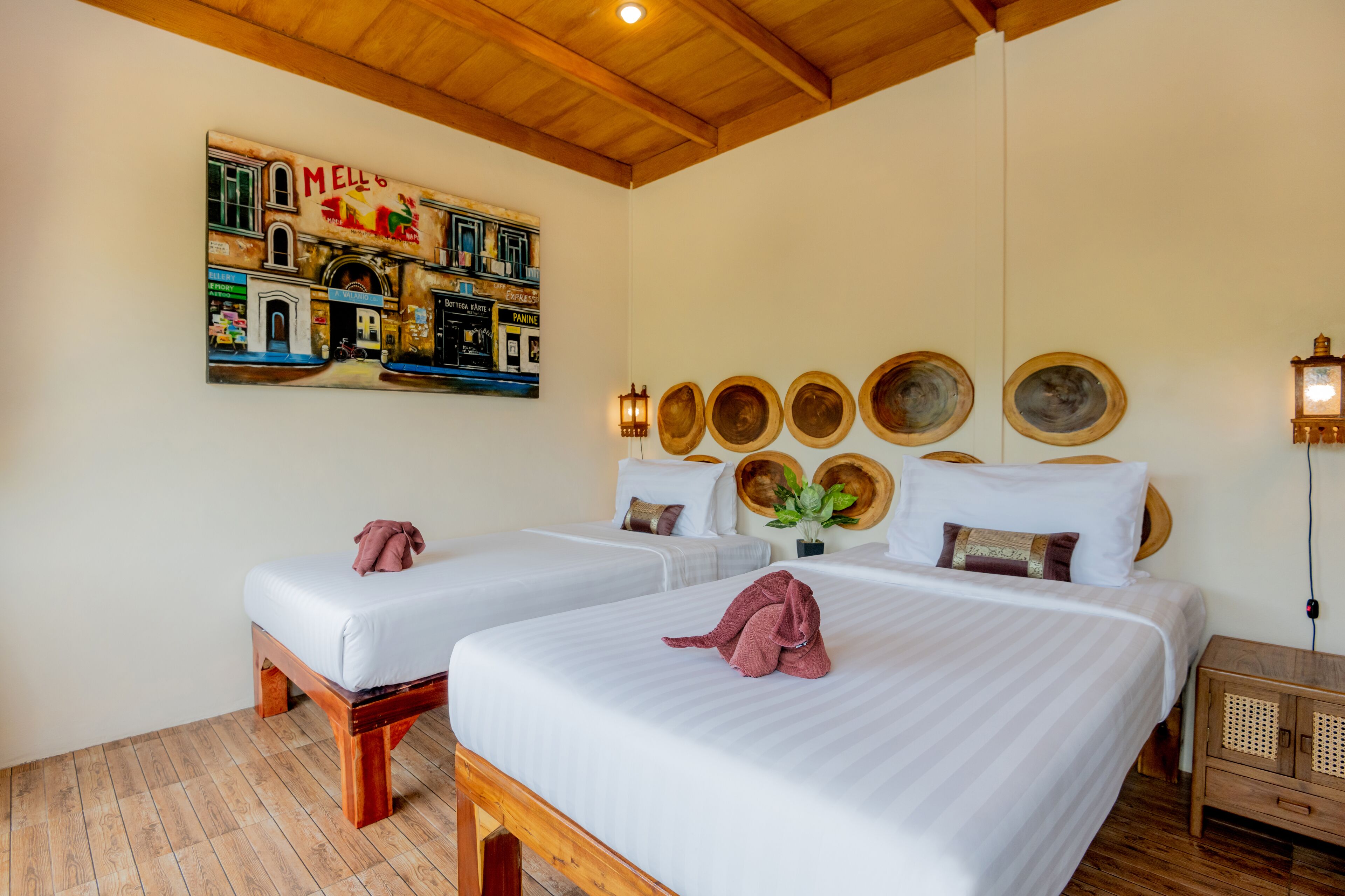 Habitación de hotel con dos camas, cabeceros de madera, lámparas, un mural en la pared y una mesita de noche de madera.