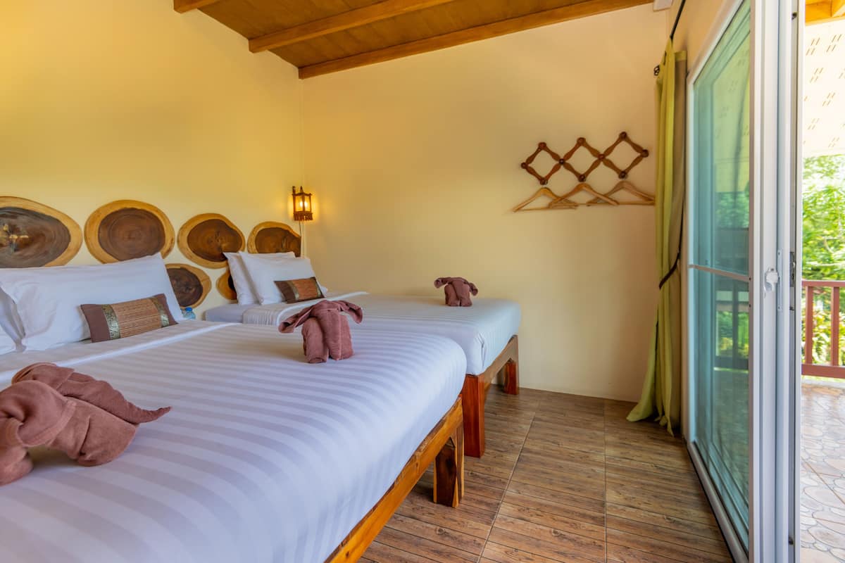 Een hotelkamer met twee bedden, houten hoofdeinden en een grote glazen schuifdeur naar een balkon.