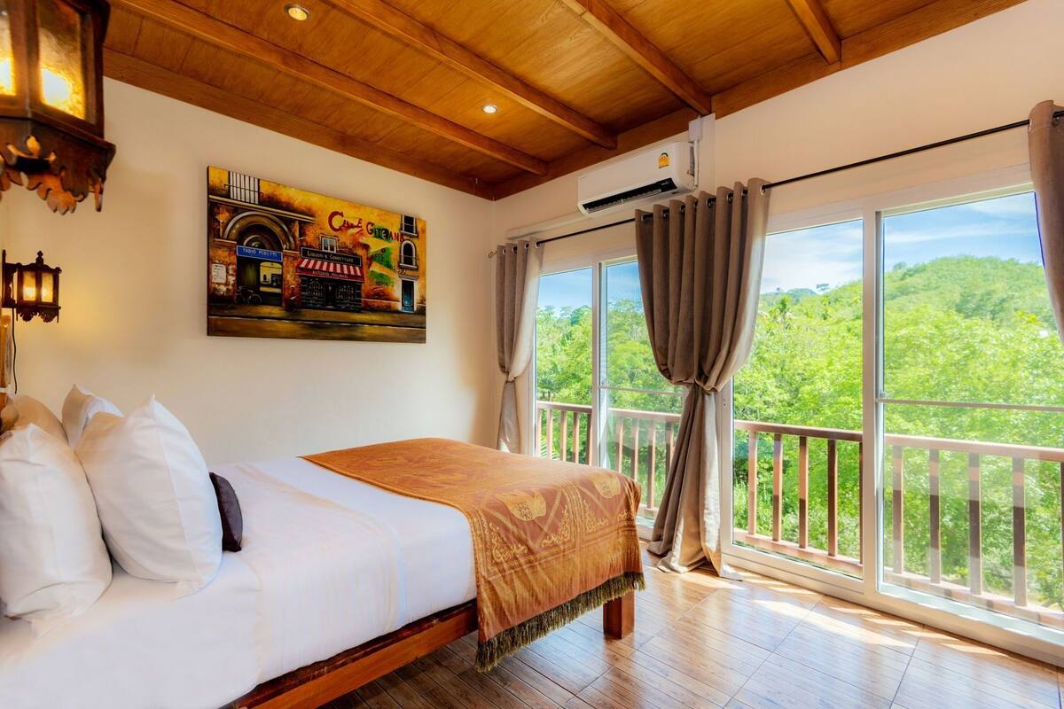 Een slaapkamer met een bed, een schilderij, een airconditioning en een balkon met uitzicht.