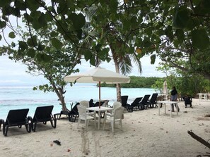 A beachside seating area with lounge chairs and tables under umbrellas, overlooking the ocean. - Surf Deck (Thulusdhoo Island)