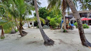 A sandy area with palm trees and a building with a red umbrella.