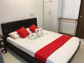 A neatly made bed with white and red bedding, a black headboard, and a wooden nightstand with a lamp. - Surf Deck (Thulusdhoo Island)