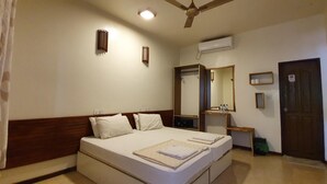 A hotel room with a bed, a ceiling fan, an air conditioning unit, a mirror, a door, and a small table with toiletries.