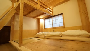 Une pièce avec un plafond en bois, un sol recouvert de tatamis, un futon servant de lit et une fenêtre à panneaux coulissants de style shoji.