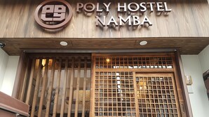 L’extérieur de l’auberge de jeunesse Poly Hostel Namba, avec sa façade en bois et une enseigne au-dessus de l’entrée.