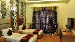 A hotel room with two beds, a desk, a television, and a decorative curtain. - Hari's Court, Lajpat Nagar (New Delhi)