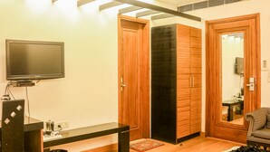 A room with a television on a stand, a wooden door, a black sliding door, and a striped sofa. - Hari's Court, Lajpat Nagar (New Delhi)