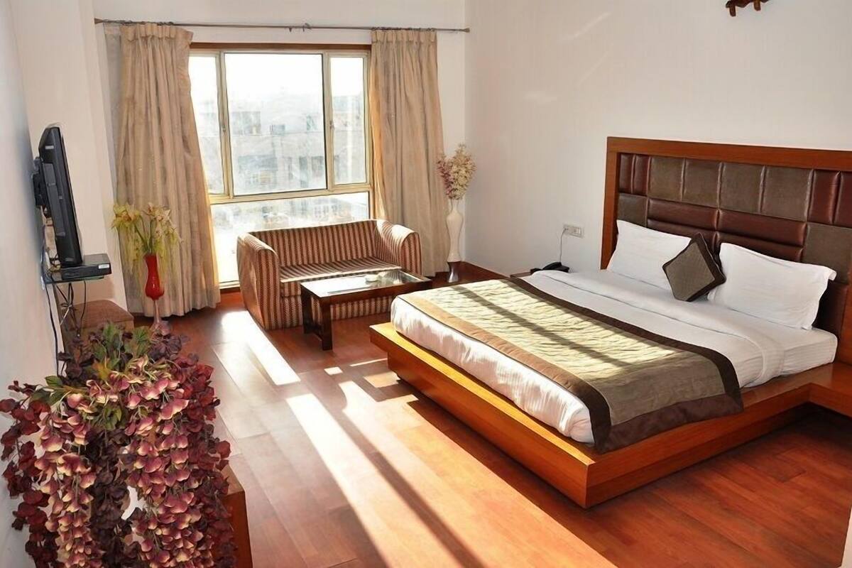 A hotel room with a large bed, a sofa, a small table, and a window with curtains.