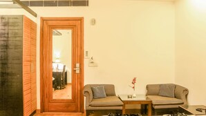 A room with a wooden door, a mirror, two striped sofas, a small table, and a vase with flowers. - Hari's Court, Lajpat Nagar (New Delhi)