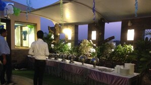 A covered outdoor dining area with a long table set for a meal, surrounded by plants and under a canopy. - Hari's Court, Lajpat Nagar (New Delhi)