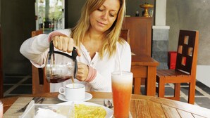 A person pouring a beverage into a cup at a wooden table with a tray of food and a glass of iced tea. - D' Padang (Pecatu)
