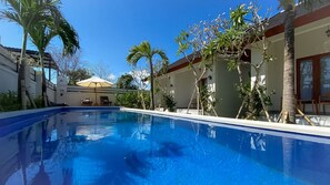 Una piscina con acqua cristallina e blu, circondata da palme e da un edificio con tetto in tegole.