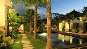 A pool area with a stone pathway, palm trees, and lounge chairs. - D' Padang (Pecatu)