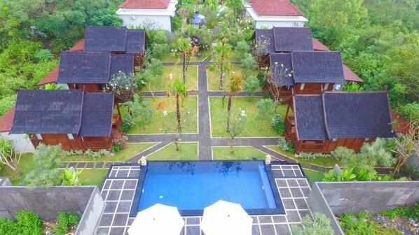 A resort with multiple wooden bungalows, a central pool, and a well-maintained garden.